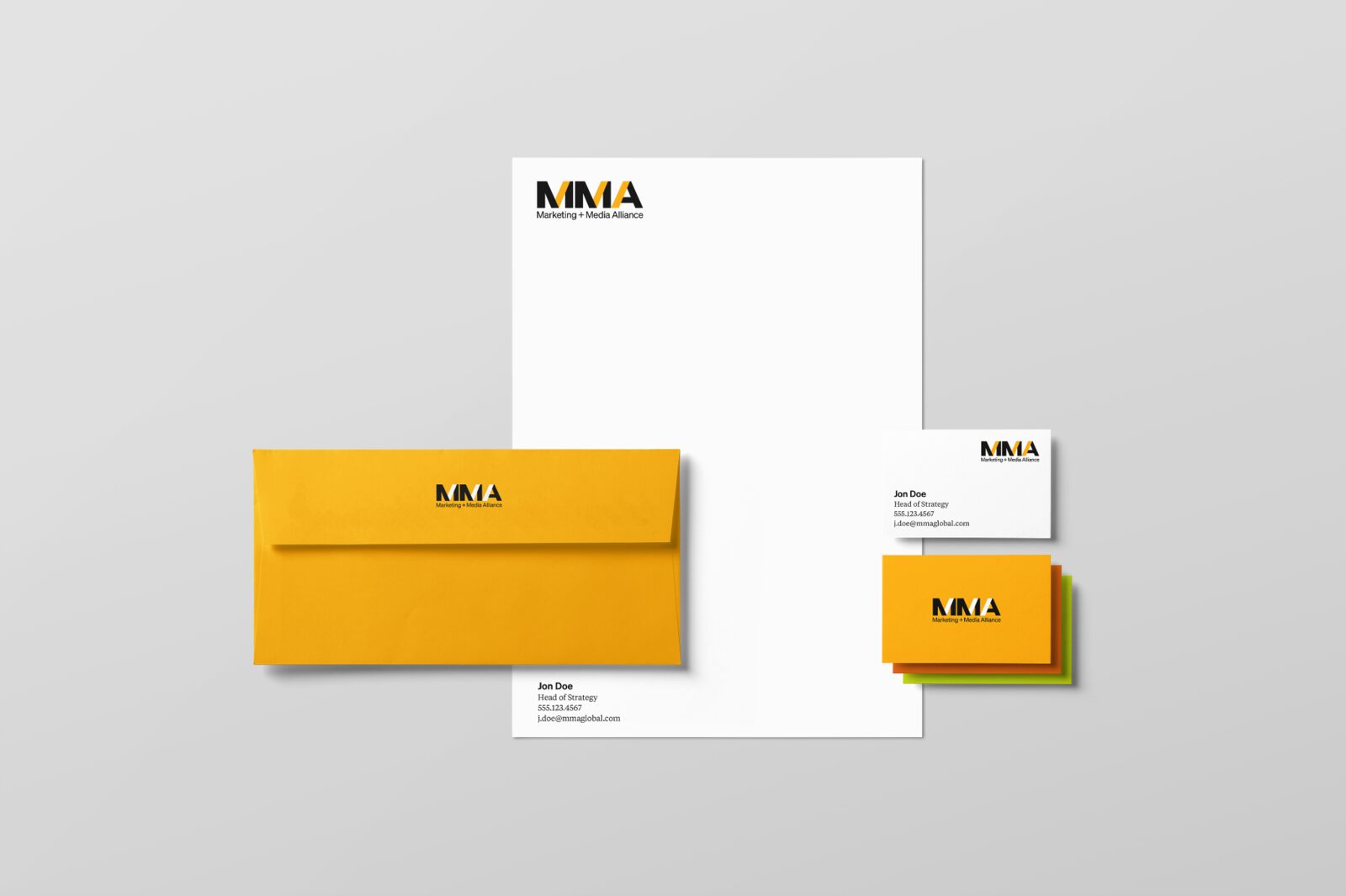 Stationery mockup: a white letterhead with the MMA logo at the top left; a gold envelope with the black and white MMA logo on the flap; white and gold business cards